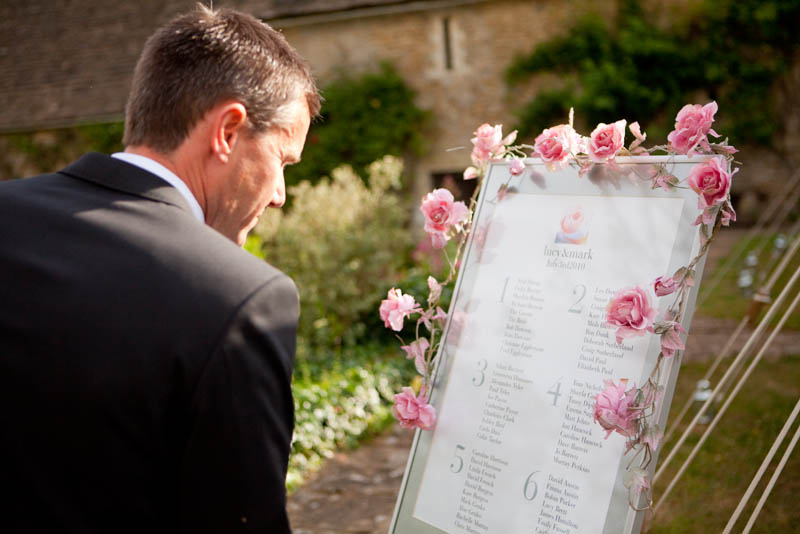 A wedding guest looks at the seating plan decorated with pink roses at Sheldon Manor wedding venue in Chippenham