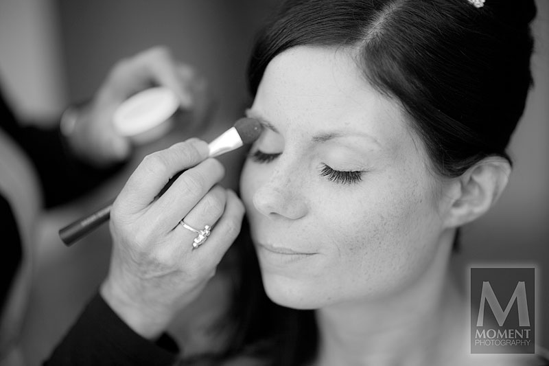 A black and white photo of a bride having makeup applied before her wedding