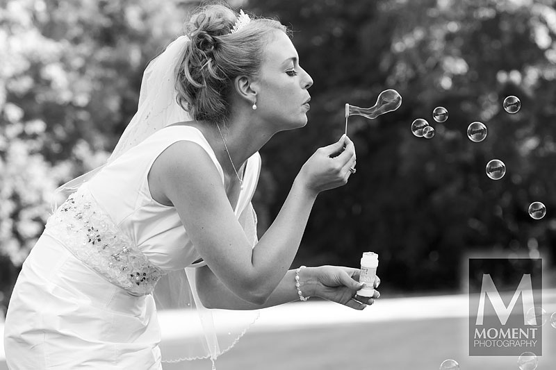 A black-and-white photo of an attractive bride blowing bubbles at Lakeview Manor in Honiton