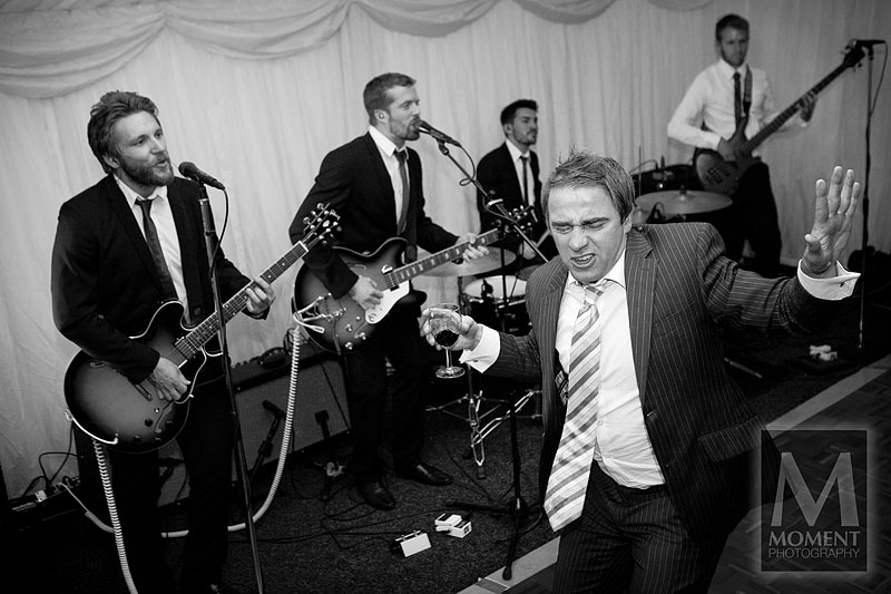 A black-and-white photo of a wedding guest dancing on the dancefloor in front of a live band