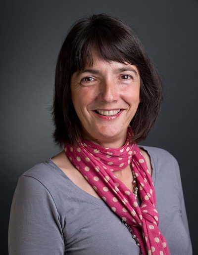 Staff business headshot of woman with black hair wearing grey top with a red scarf